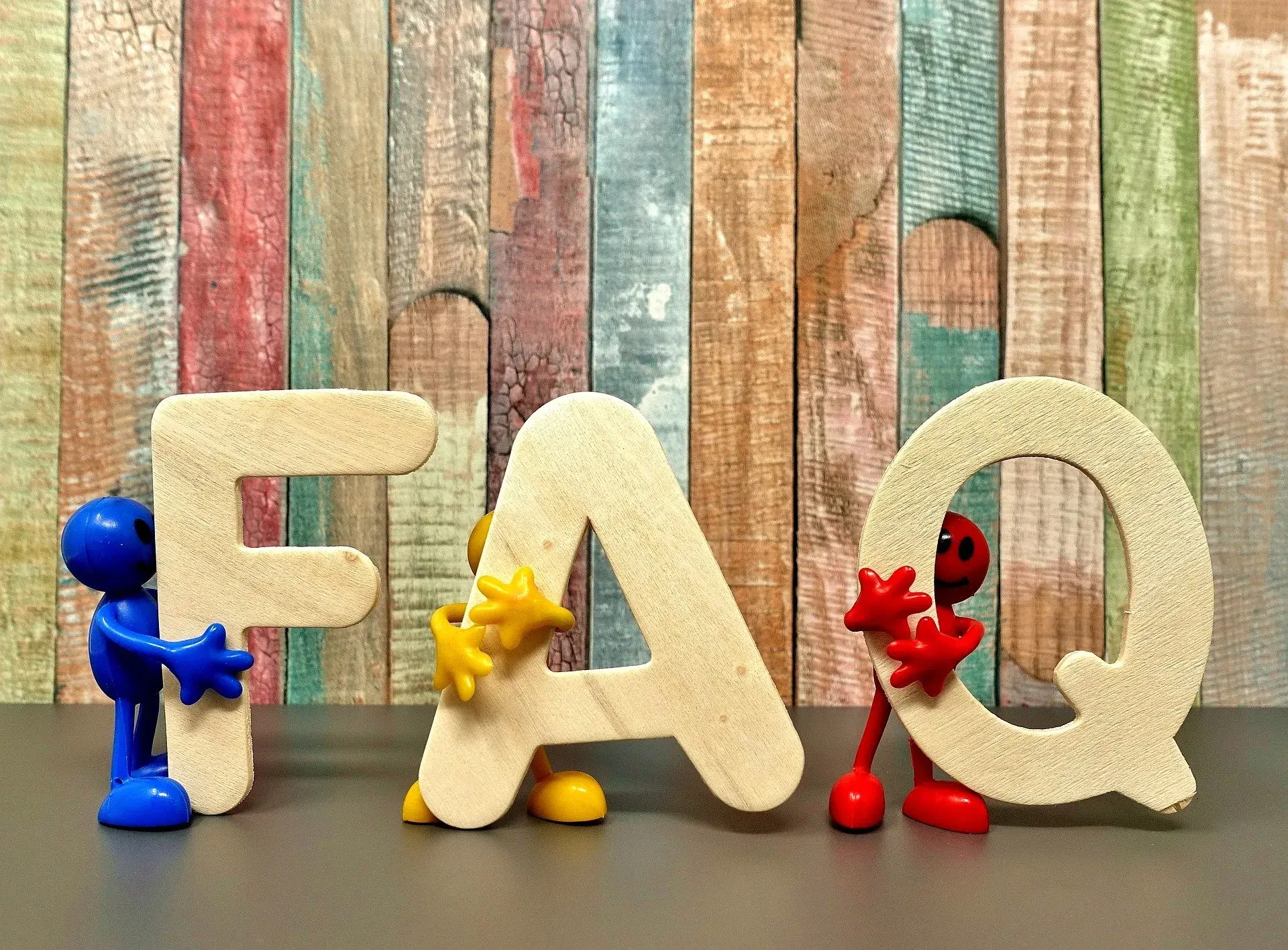 Wooden FAQ letters held by colorful toy figures | AIGente